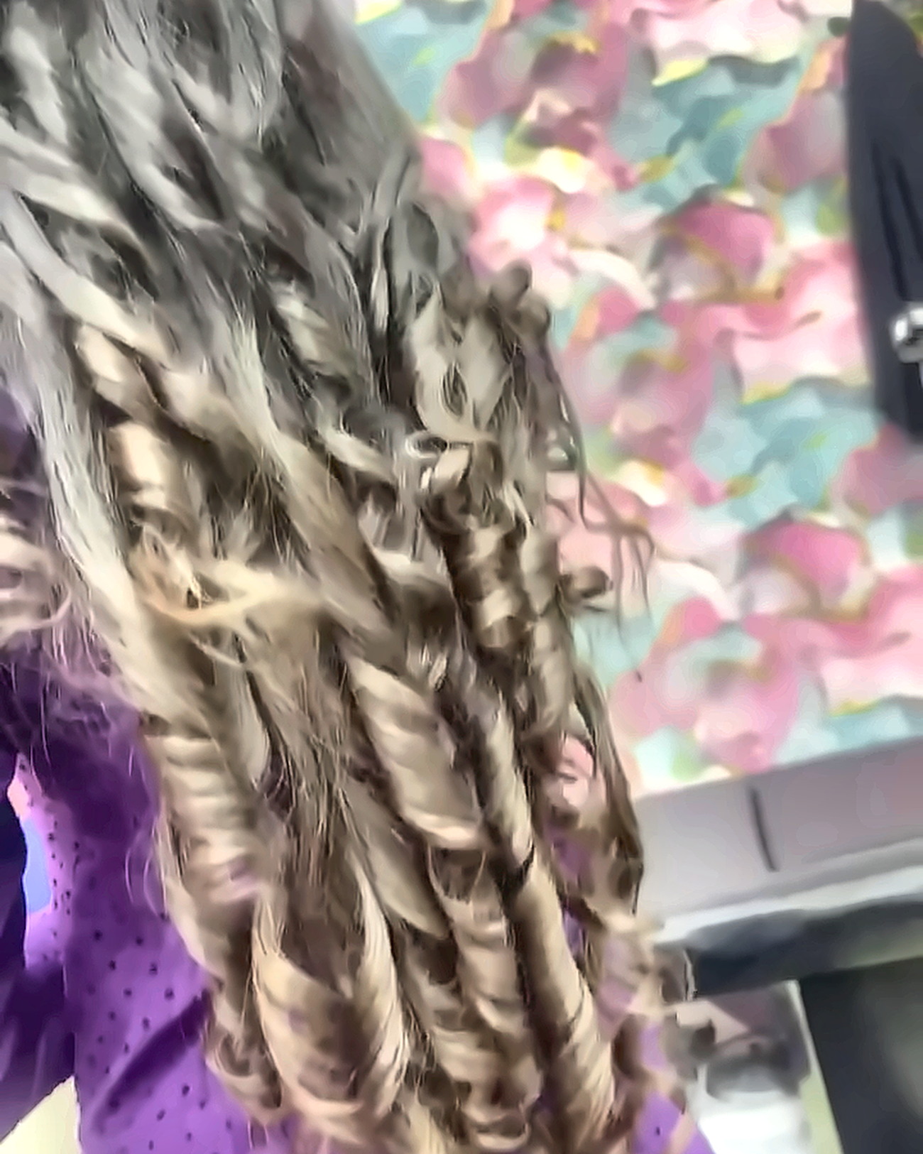 Long ash-blonde hair set into defined spiral curls with tongs, in front of the salon's pink and turquoise floral wall