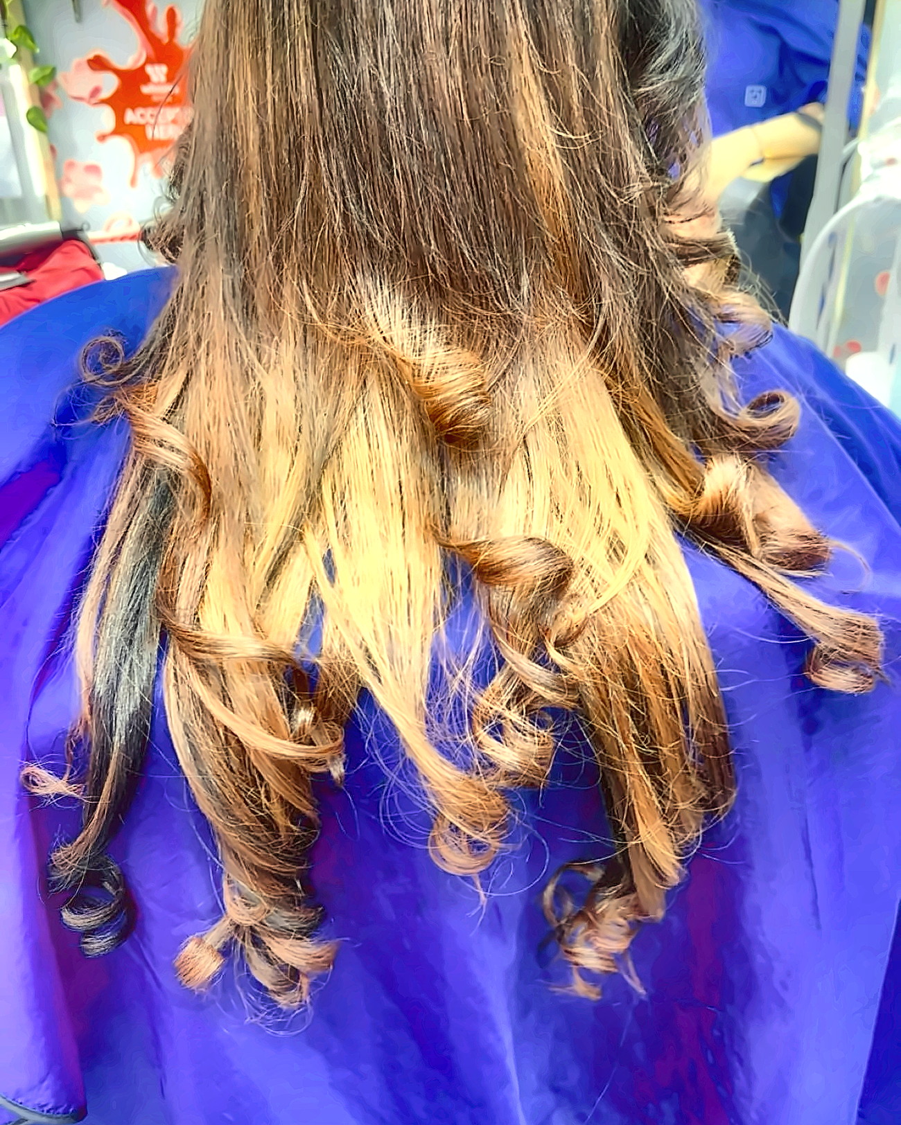Caramel ombré hair curled into loose ringlets over a blue salon cape