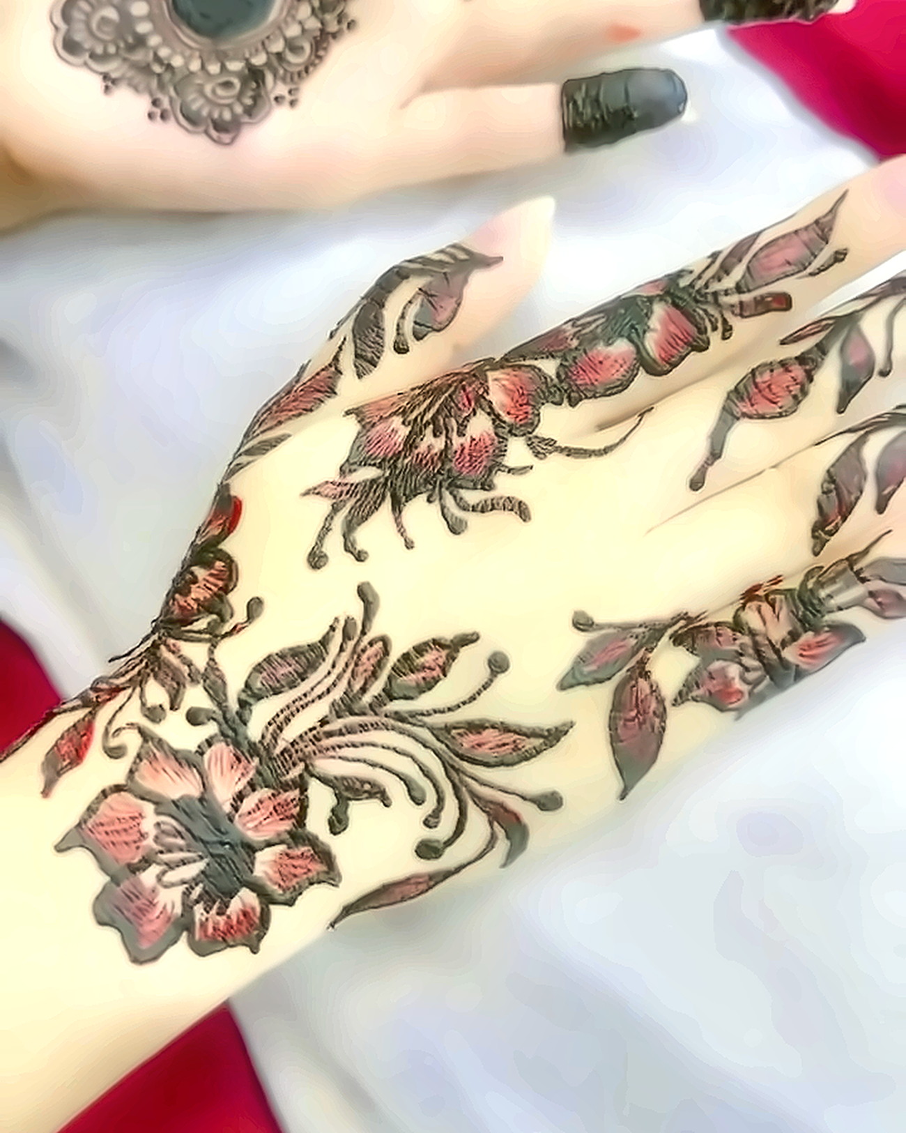 Hand and forearm painted with fine-line floral henna, petals shaded in rose against fresh dark paste