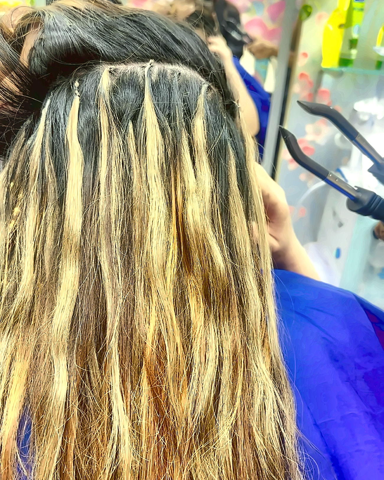 Micro-bonded blonde hair extensions being fitted strand by strand into dark natural hair