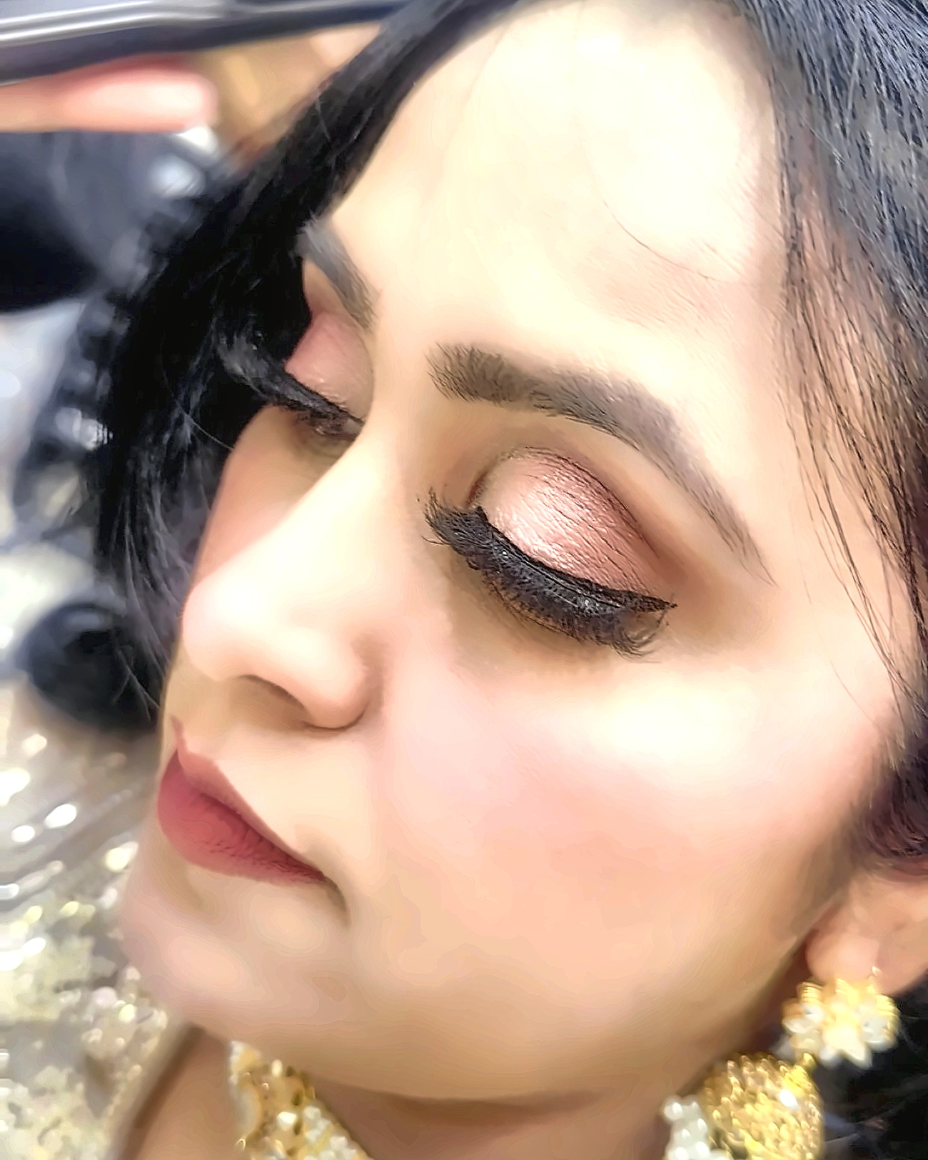 Rose-gold metallic eyeshadow and sharp black liner being finished on a guest's eye at the styling chair