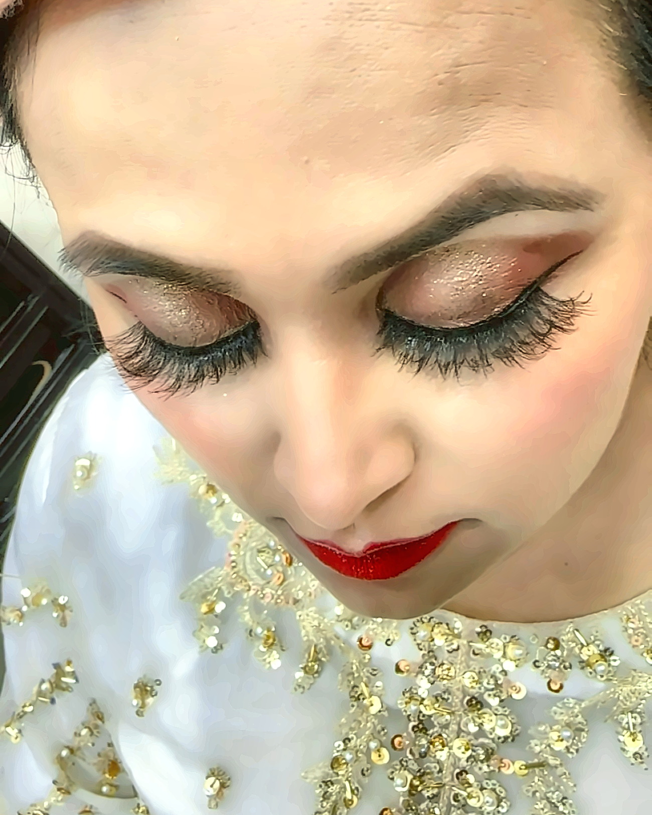 Bride with smoked bronze glitter eyeshadow, winged liner, full lashes and red lips, wearing a gold-embroidered white dupatta