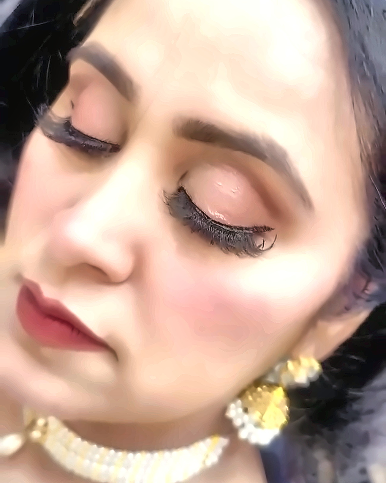 Guest with soft matte base, black winged liner, strip lashes and a rose-brown lip, wearing pearl and gold jewellery