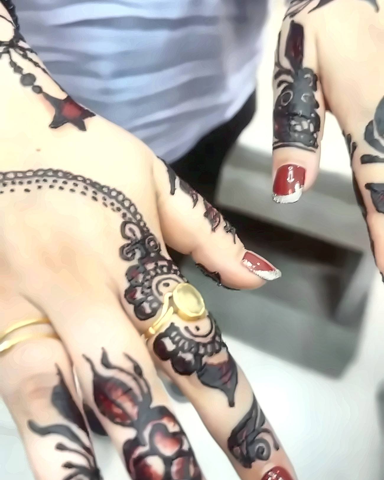 Two hands painted with bold black-and-maroon henna panels, worn with gold rings and dark red French nails